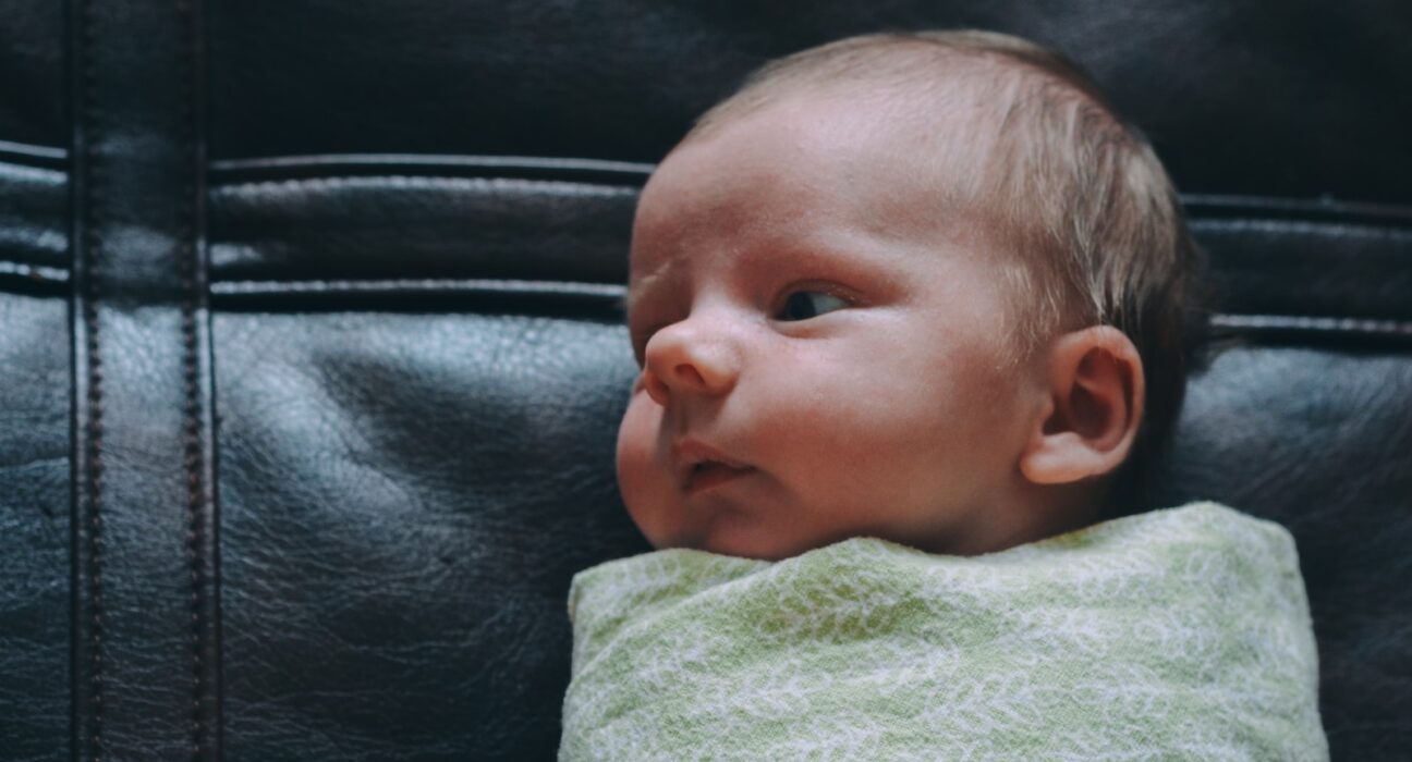 baby covered in green blanket on black leather surface