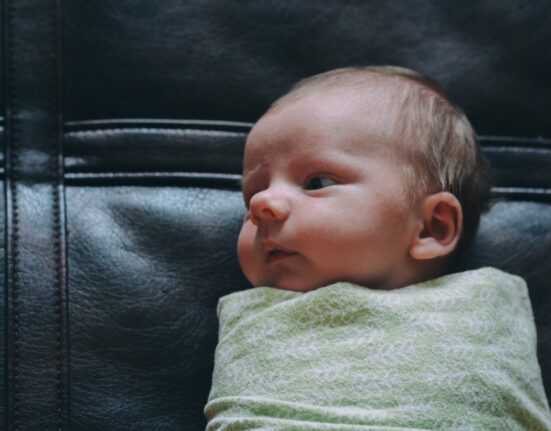 baby covered in green blanket on black leather surface
