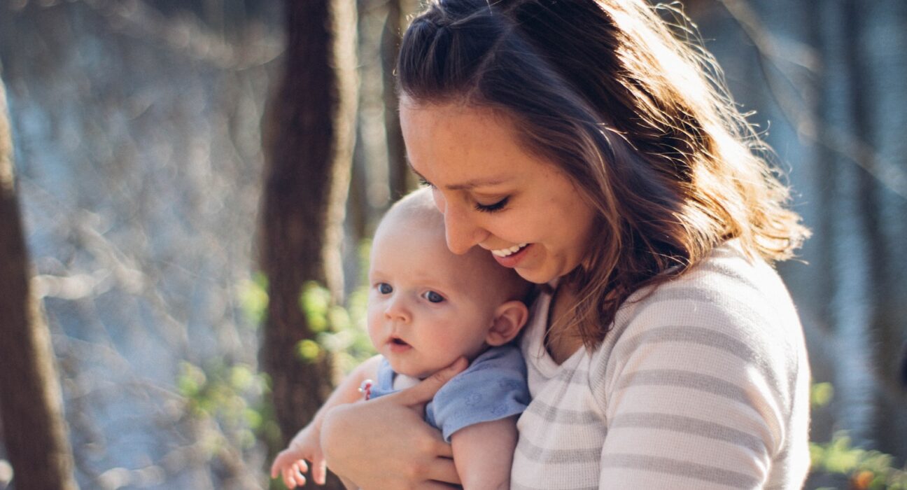woman carrying baby near trees