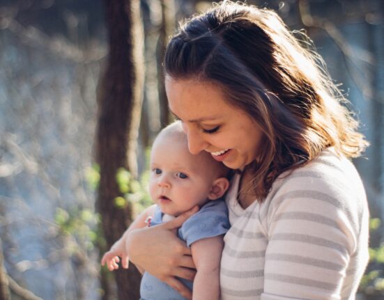 woman carrying baby near trees