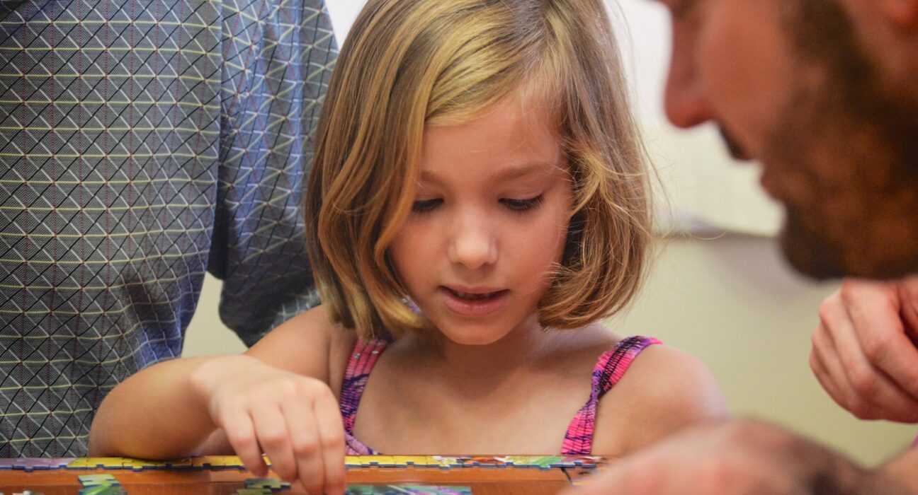 girl in blue and white polka dot tank top playing on brown wooden table