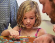 girl in blue and white polka dot tank top playing on brown wooden table
