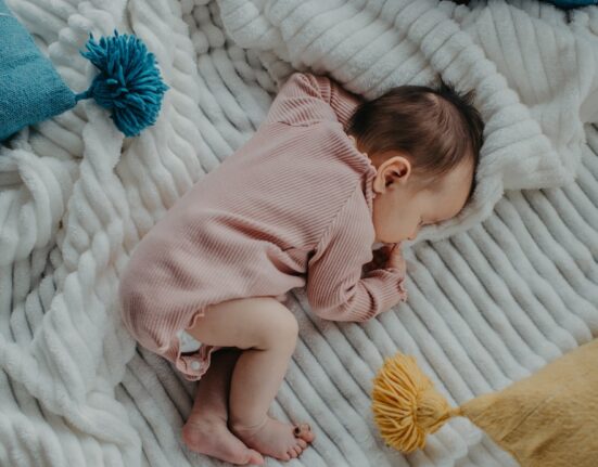 baby in pink onesie lying on white bed