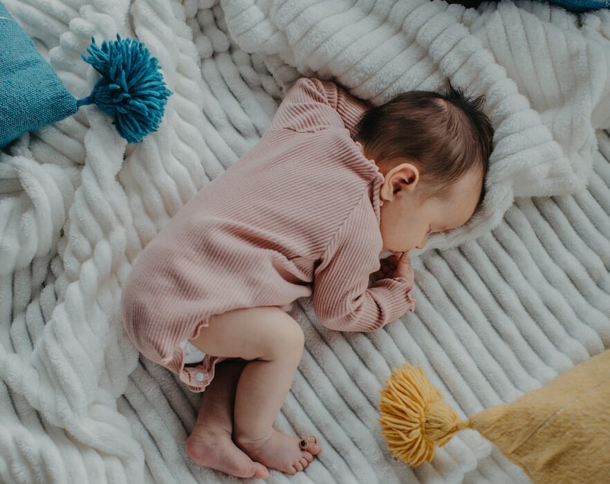 baby in pink onesie lying on white bed