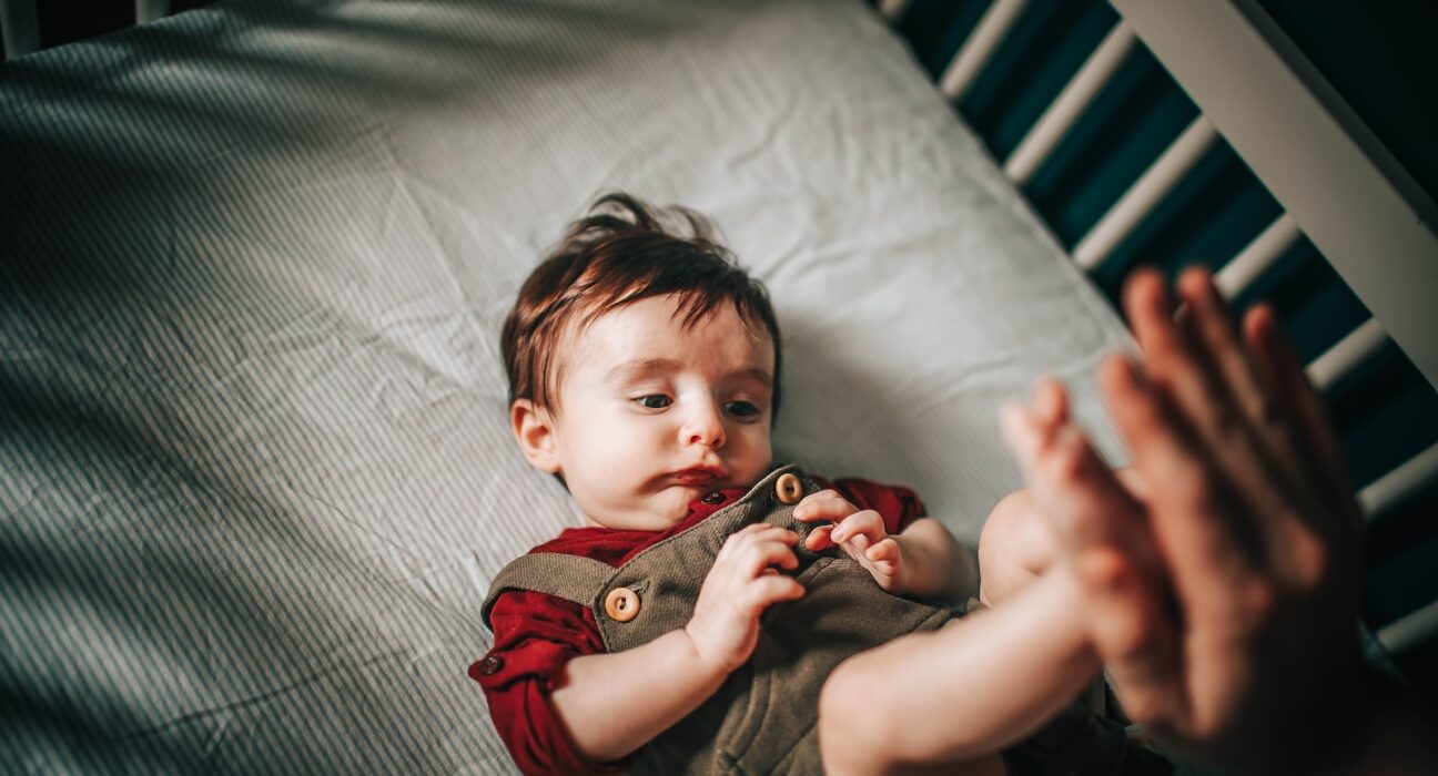 baby in gray shirt lying on bed