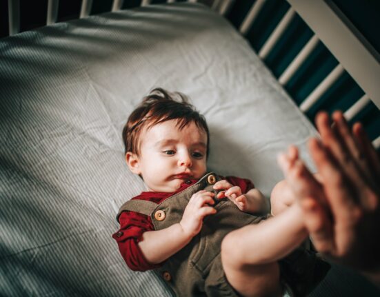 baby in gray shirt lying on bed