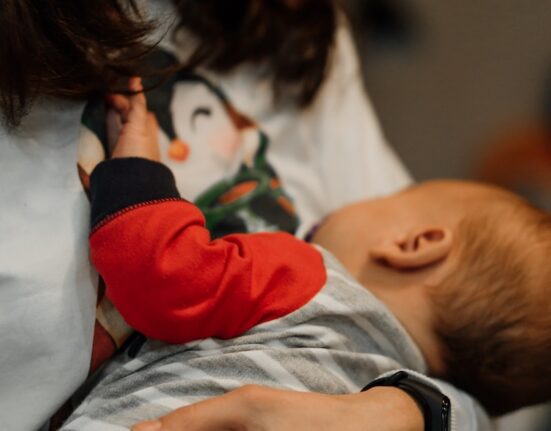 woman in white long sleeve shirt carrying baby in red and white long sleeve shirt
